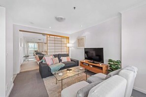 Ein modernes Wohnzimmer mit einer Couch, einem Glastisch, einem Fernseher und einer Pflanze.