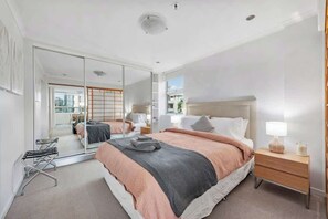 Ein modernes Schlafzimmer mit einem großen Bett, einem Nachttisch, einem Spiegel und Blick auf die Stadt.