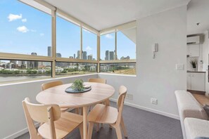 Ein modernes Zimmer mit einem runden Tisch, vier Stühlen, einer kleinen Pflanze und Blick auf die Stadt durch große Fenster.