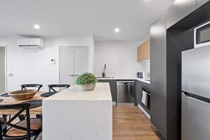 A modern kitchen with a central island, built-in appliances, and a dining area with chairs and a table. - Stylish & Slick! 1bed/1bath/1car ~ Walk to CBD (Brisbane)