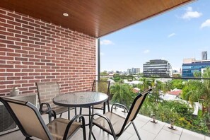 A balcony with a brick wall, a round table, and chairs, overlooking a cityscape. - Stylish & Slick! 1bed/1bath/1car ~ Walk to CBD (Brisbane)