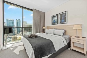 Ein Hotelzimmer mit großem Fenster, einem Bett, einem Nachttisch und einem an der Wand befestigten Fernseher.