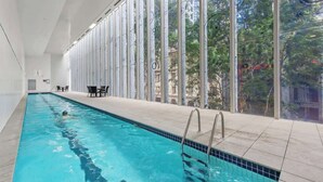 An indoor swimming pool with clear glass walls, a tiled floor, and a view of greenery outside. - City Centre! 1bed/1bath/study/1car/balcony ~ CBD (Brisbane)