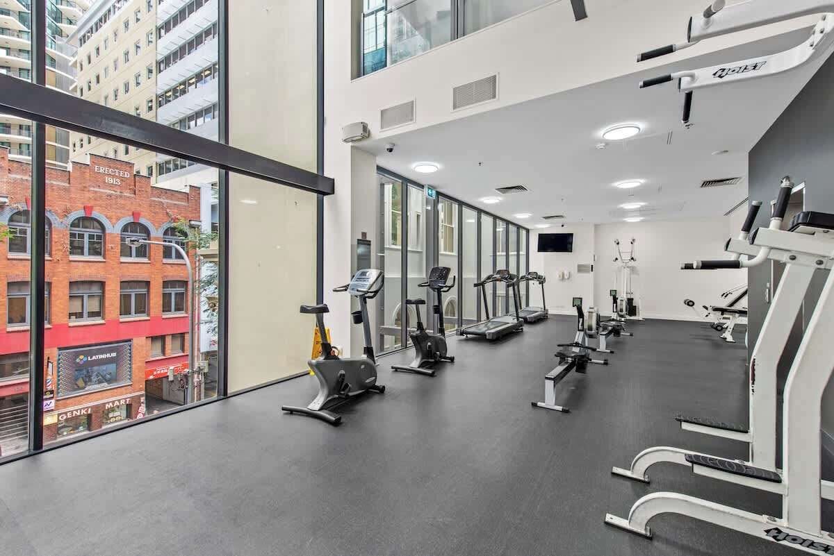 Ein Fitnessstudio mit verschiedenen Trainingsgeräten, großen Fenstern und Blick auf ein rot backsteins Gebäude.