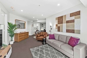 A modern living room with a sofa, a coffee table, a TV, a wooden cabinet, a mirror, and a plant. - Infinity Excellence!~1bed/1bath/office/1car~views! (Brisbane)