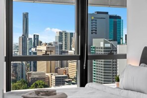A hotel room with a large window offering a city view, a bed, and a small plant on the windowsill. - Infinity Excellence!~1bed/1bath/office/1car~views! (Brisbane)