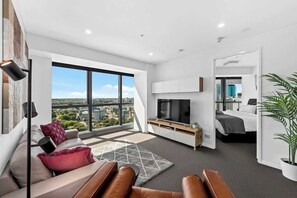 Een moderne hotelkamer met een groot raam, een flatscreen televisie, een bank, een bed en een kamerplant.