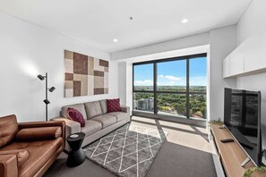 Ein modernes Wohnzimmer mit einer Couch, einem Couchtisch, einem Fernseher und einem großen Fenster mit Blick auf die Stadt.