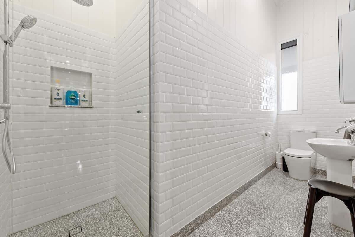 A bathroom with white subway tile walls, a shower, a toilet, and a sink.