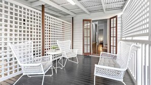A covered outdoor area with white wicker furniture, a wooden table with a plant, and a view into an adjacent room through a glass door. - The Deck! 2 Bed/1 Bath/1 Car ~ New Farm (Brisbane)
