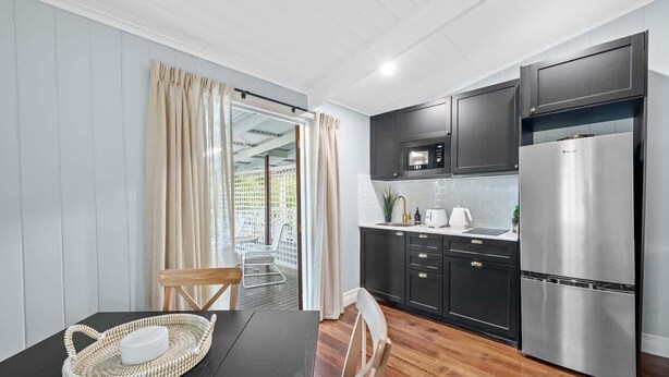 A modern kitchen with dark cabinets, a stainless steel refrigerator, and a dining area with a table and chairs. - The Deck! 2 Bed/1 Bath/1 Car ~ New Farm (Brisbane)