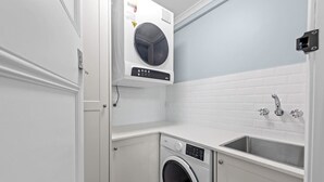 A compact laundry room with a front-loading washing machine, a sink, and a tiled backsplash. - The Deck! 2 Bed/1 Bath/1 Car ~ New Farm (Brisbane)