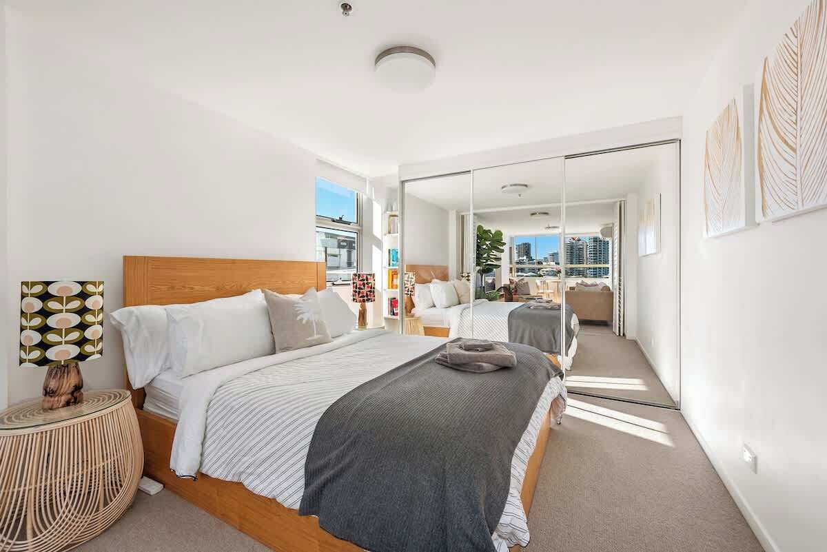A modern bedroom with a large bed, a bedside lamp, and a view of the city through a glass door.
