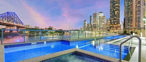 A swimming pool with a city skyline and a bridge in the background.