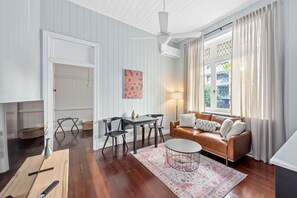 Ein Zimmer mit Deckenventilator, braunem Ledersofa, Esstisch mit Stühlen und einem gemusterten Teppich.