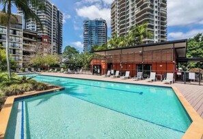 Ein Pool mit Liegestühlen, umgeben von hohen Gebäuden und Palmen.