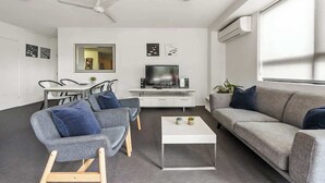 Ein modernes Wohnzimmer mit einer Couch, Sesseln, einem Couchtisch, einem Fernseher und einem Deckenventilator.