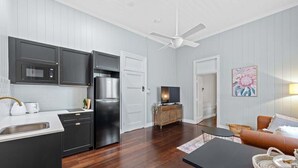 A modern kitchen with dark cabinets, a refrigerator, and a microwave. There is a dining area with a table and chairs, and a living room with a sofa and a television. - The Office! 1 Bed/1 Bath ~ New Farm (Brisbane)