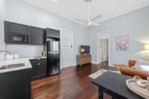 Eine moderne Küche mit dunklen Schränken, einem Kühlschrank und einer Mikrowelle. Ein Essbereich mit Tisch und Stühlen lädt zum Verweilen ein, und ein Wohnzimmer bietet eine Couch und einen Fernseher.