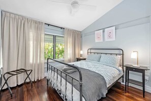 Ein Schlafzimmer mit einem Bett, einem Nachttisch, einer Lampe, einem Deckenventilator und einem Fenster mit Vorhängen.