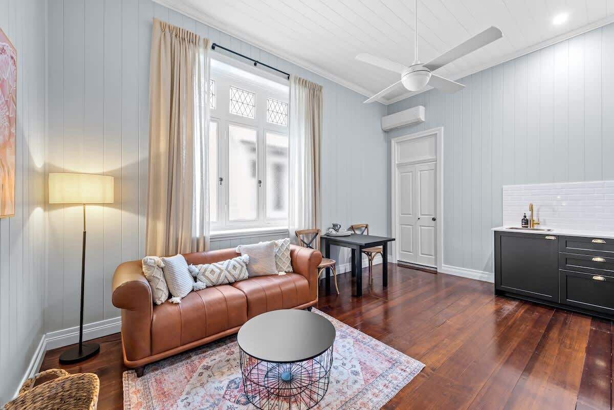 A living room with a leather sofa, a round coffee table, a dining table, and a kitchen area with a black cabinet.