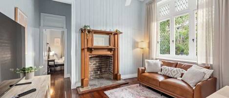 A room with a fireplace, a leather sofa, a wooden coffee table, and a large window with curtains.