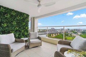 A balcony with wicker furniture, a green wall, and a city view. - Stunning! 2bed, 1bath, 1car, Views ~ CBD (Brisbane)