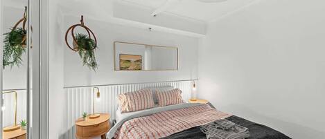 Un dormitorio con cama, mesitas de noche, ventilador de techo, espejo y ventana.