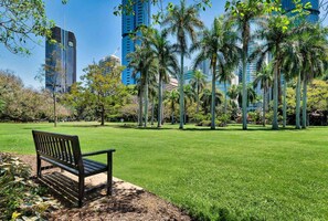 A park with a bench, palm trees, and modern buildings in the background. - Stunning! 2bed, 1bath, 1car, Views ~ CBD (Brisbane)