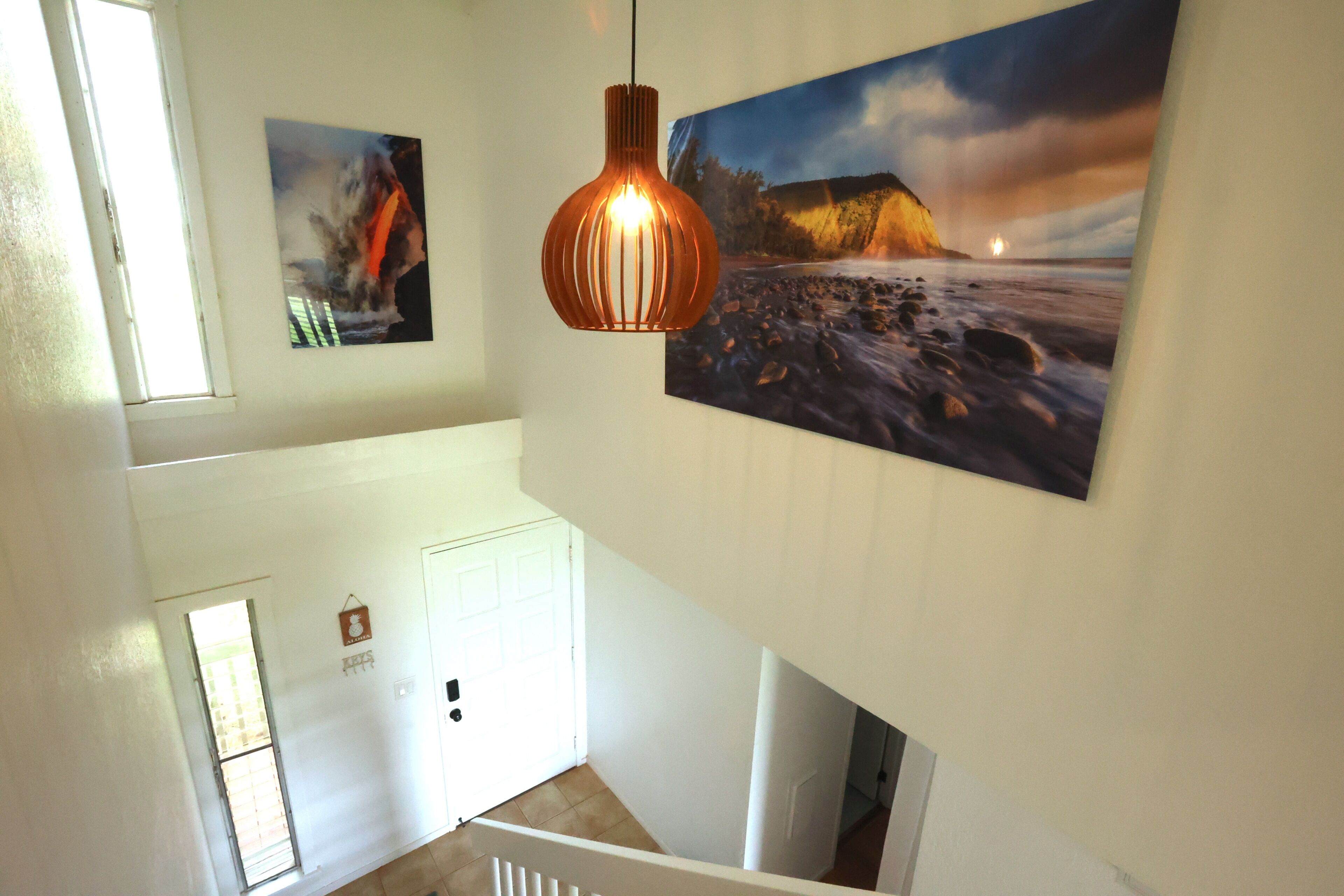 A staircase with a view of a beach scene and a sunset painting on the wall.