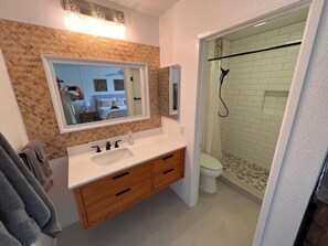 A bathroom with a wooden vanity, a large mirror, a shower with a glass door, and a tiled floor. - Beautiful Spacious Ocean and Mountain View Condo Kauai, Hawaii (Princeville)