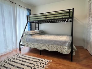 Een stapelbed met een ladder, een bed met een patroon erop en een geweven vloerkleed op een houten vloer.