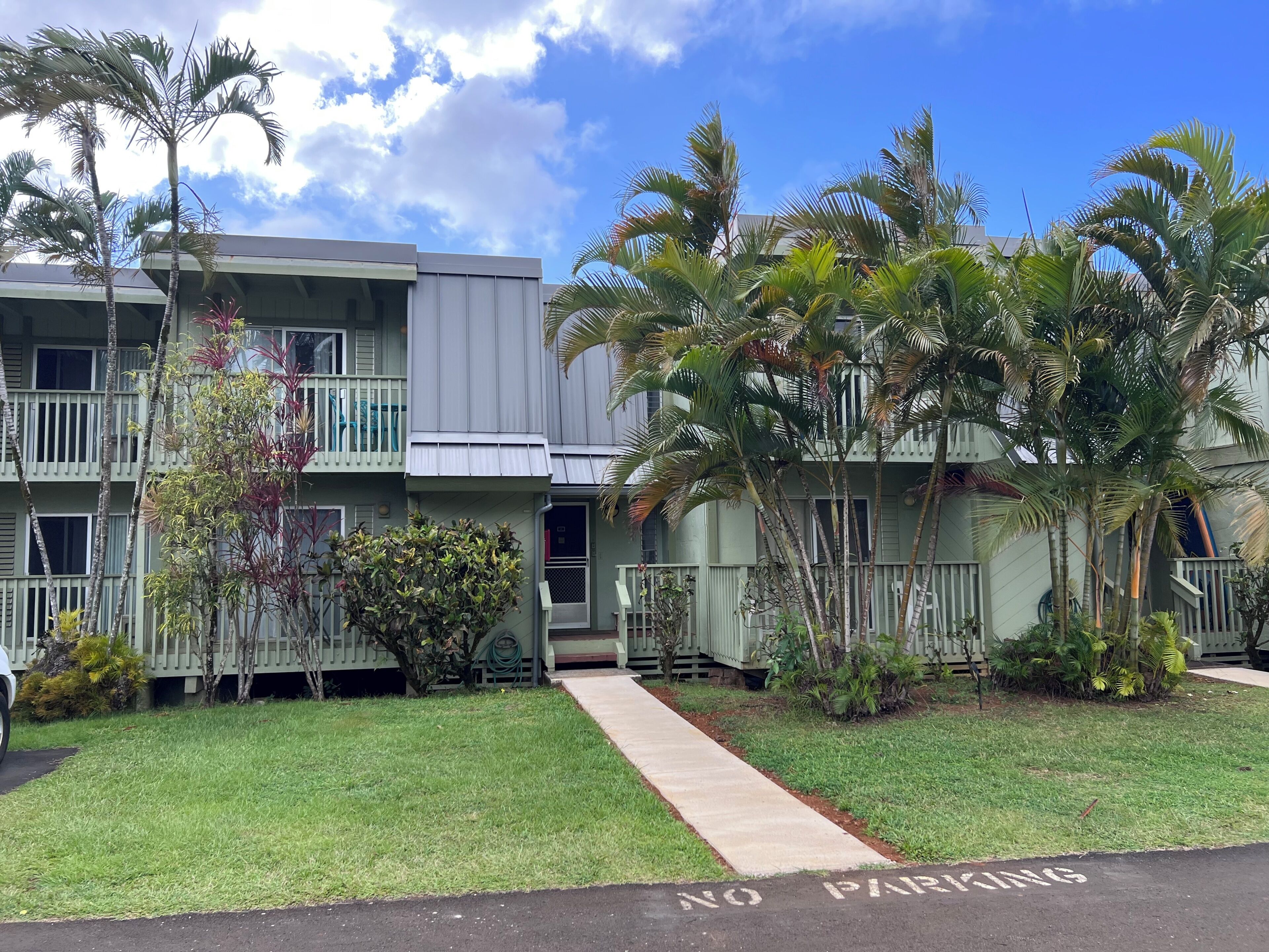 A multi-story building with balconies, surrounded by palm trees and a grassy area.
