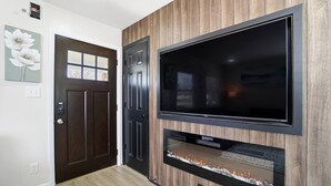 A hallway with a dark wooden door, a wall-mounted flat-screen TV, and a built-in fireplace. - Cozy 3BR Home Close to WSU, UD & Wright-Patt AFB (Dayton)