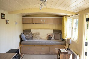 A cozy room with a built-in sofa, wooden cabinets, a small table with a lamp, and a window with curtains.