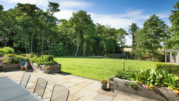 A patio area with a table and chairs, surrounded by a well-maintained lawn and a variety of plants. - Tewin Bury Farm Hotel (Welwyn)