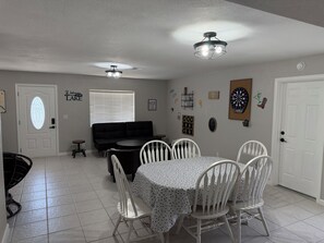 A dining area with a table and chairs, a black sofa, and a ceiling light fixture. - Lake Havasu Getaway- Private Pool-4BR -Sleeps 10- Family Fun (Lake Havasu City)