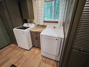 A laundry area with two washing machines, a countertop, and a window with a view of trees. - Updated cabin on the Au Sable River 10 minutes from Grayling (Grayling)