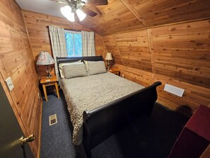 A wooden-paneled room with a bed, two bedside tables, a ceiling fan, and a window with curtains. - Updated cabin on the Au Sable River 10 minutes from Grayling (Grayling)