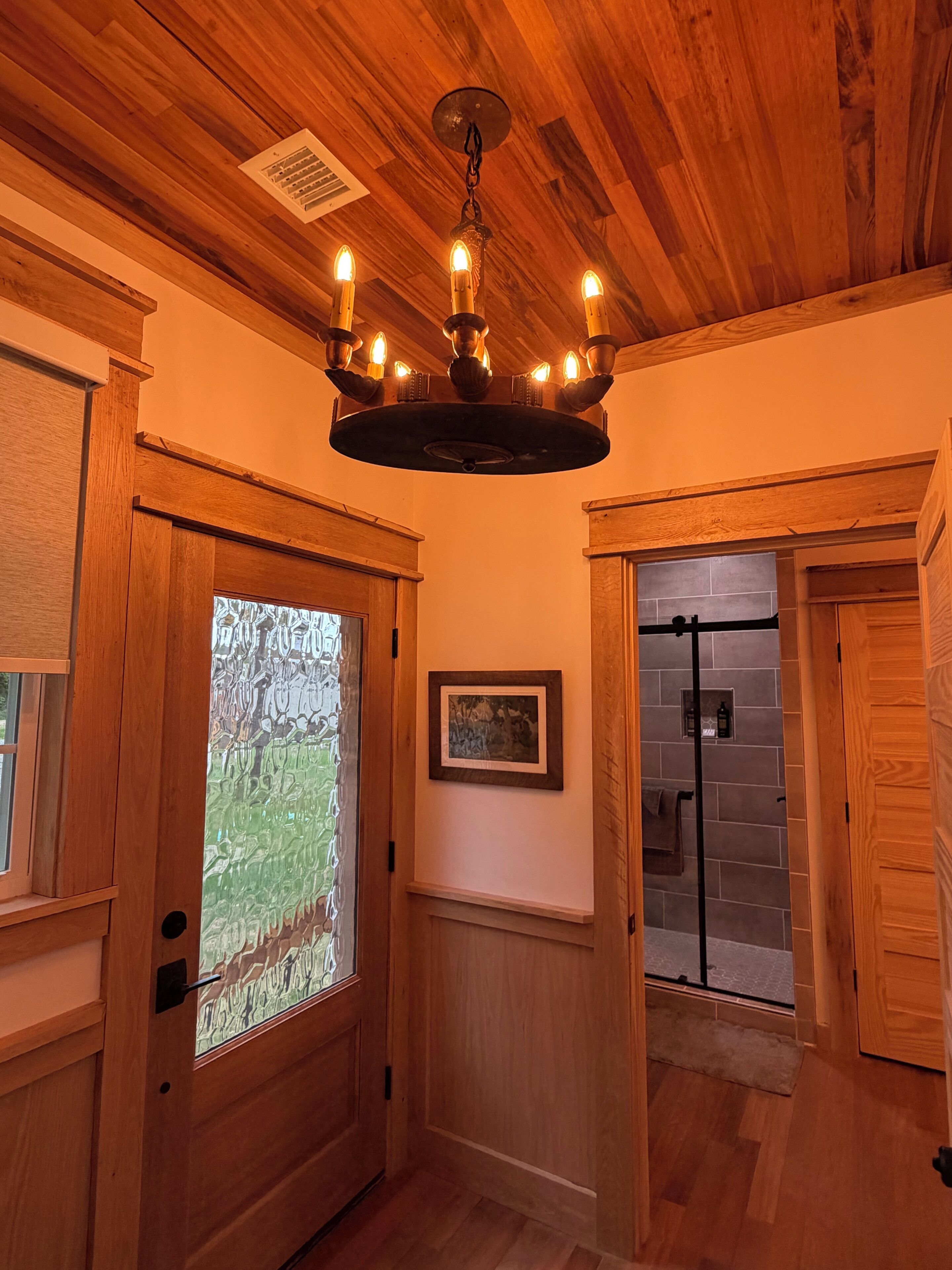Un intérieur en bois agrémenté d’un lustre, d’une porte avec un panneau en verre dépoli et d’un tableau encadré au mur.