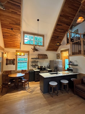A modern kitchen with a central island, wooden flooring, and a dining area with a round table and chairs. - Cozy 2-bedroom “Copper Ridge”cabin trout fishing River Access: exotic hardwoods (Gore)