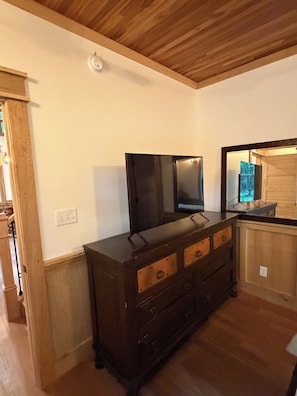A room with a wooden dresser, a flat-screen TV, and a wooden ceiling.