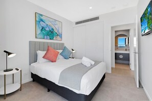 A modern hotel room with a bed, bedside lamps, a painting, and a bathroom visible through an open door. - Stunning Water View 1BR  | Steps to Casino and Tram (Broadbeach)