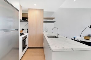 A modern kitchen with a built-in oven, a sink, and a wooden cabinet. - Stunning Water View 1BR  | Steps to Casino and Tram (Broadbeach)