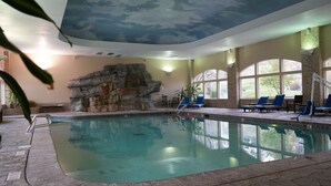 Una piscina interior con pared de piedra, sillas de descanso y ventanas amplias.