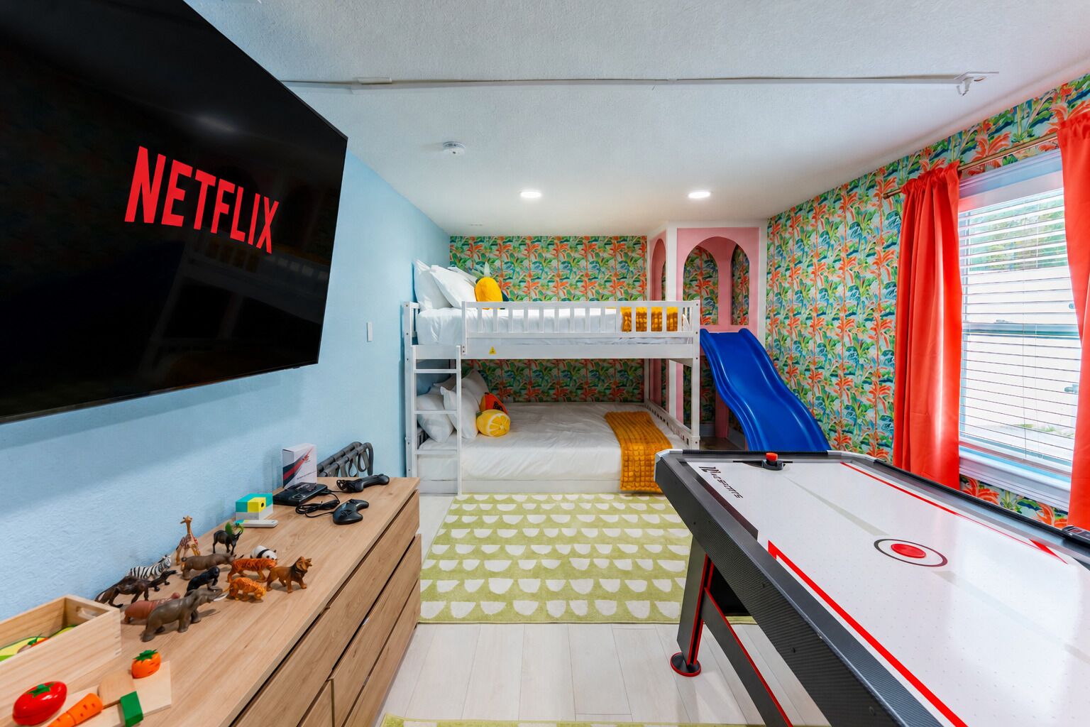 A room with bunk beds, a play area with toys, a pool table, and a TV screen displaying 'NETFLIX'.