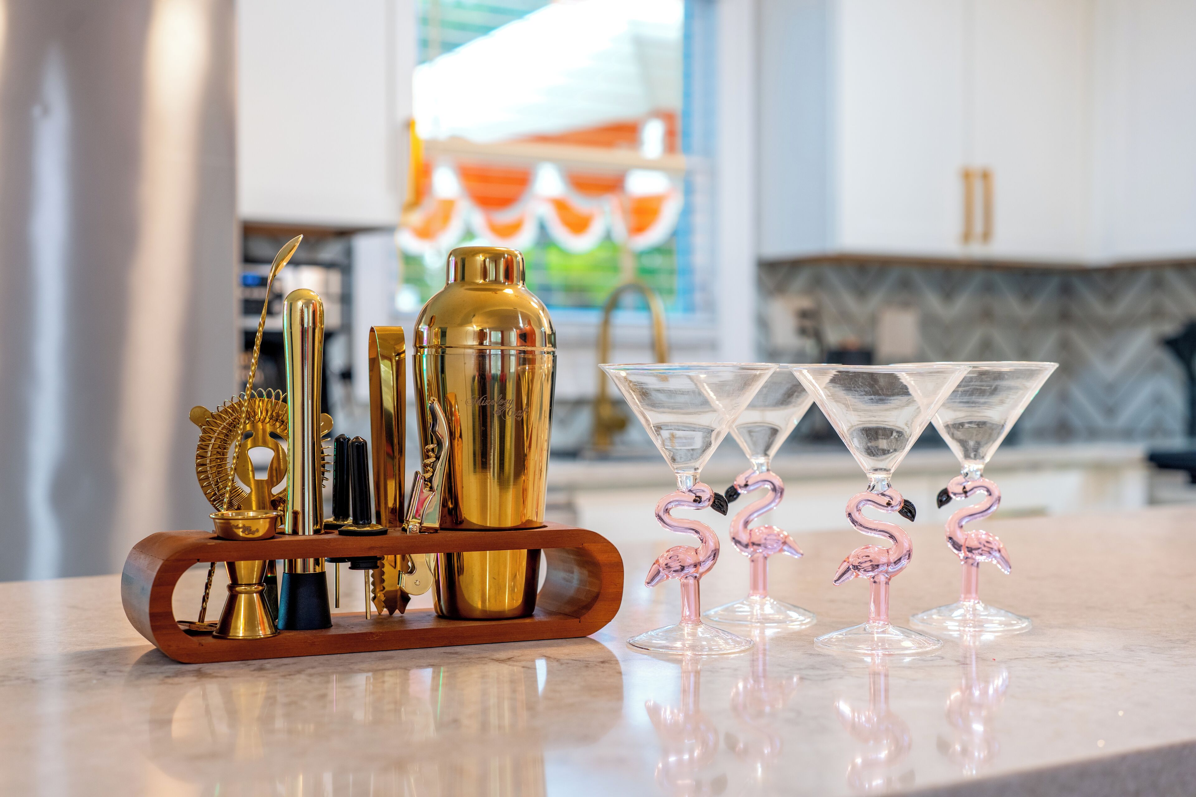 A bar area with a variety of cocktail shakers, a bottle, and a set of martini glasses with flamingo decorations.