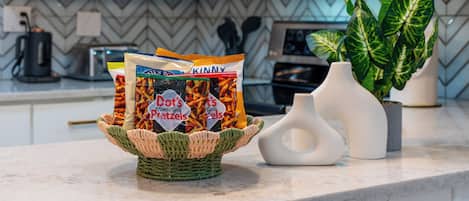 Een aanrecht met een gevlochten mand die snacks, een witte vaas en een potplant bevat.