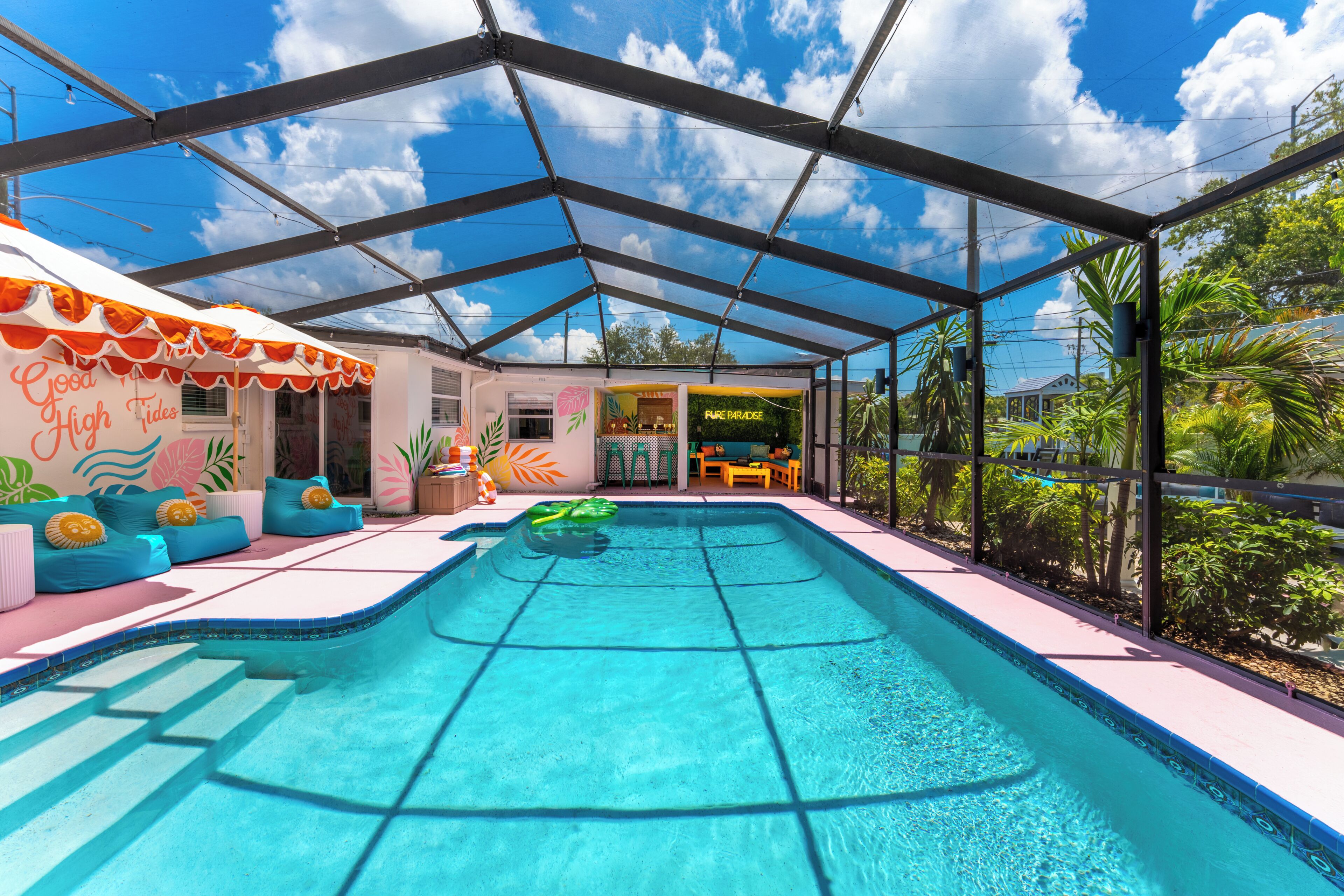 Une piscine intérieure couverte, dotée d’un toit en verre, entourée de sièges aux couleurs vives et agrémentée d’une façade aux motifs tropicaux.