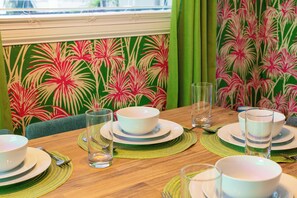 Ein Esstisch ist mit weißen Schüsseln, Tellern und Gläsern gedeckt, im Hintergrund ist eine grüne Tapete mit Muster zu sehen.